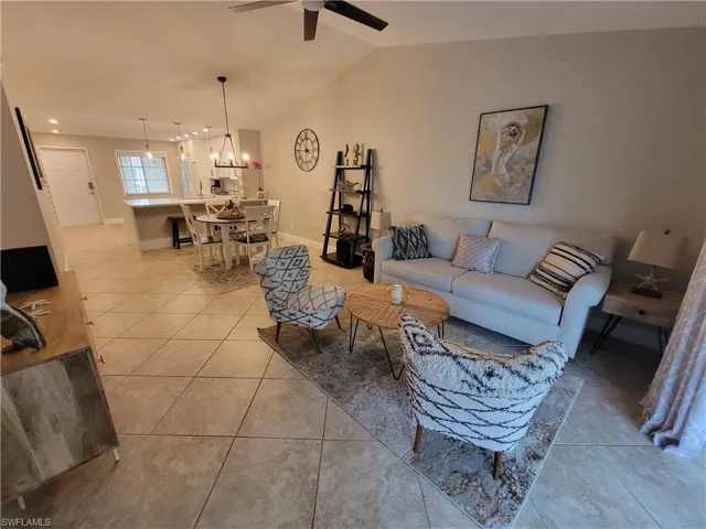 Living room with vaulted ceiling, light tile floors, and ceiling fan with notable chandelier