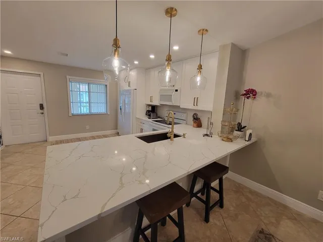 Kitchen with a kitchen breakfast bar, hanging light fixtures, white appliances, white cabinets, and kitchen peninsula