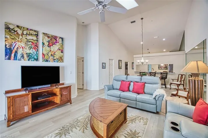 Living room with high vaulted ceiling, light wood-style flooring, ceiling fan, a skylight, and a chandelier