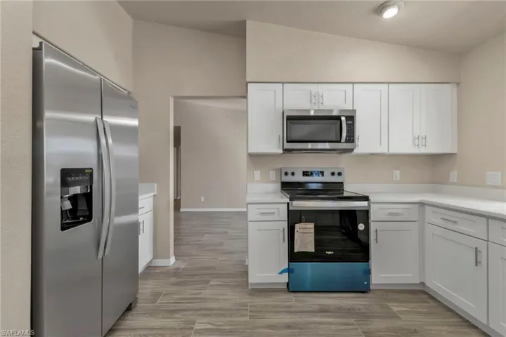 Kitchen with white cabinets, appliances with stainless steel finishes, and vaulted ceiling