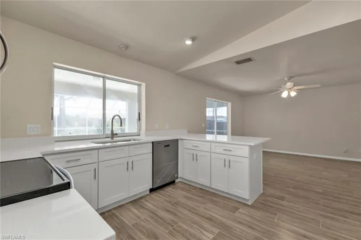 Kitchen featuring kitchen peninsula, sink, stainless steel dishwasher, ceiling fan, and white cabinetry