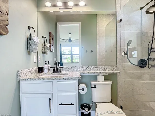 Bathroom featuring a tile shower, ceiling fan, vanity, and toilet