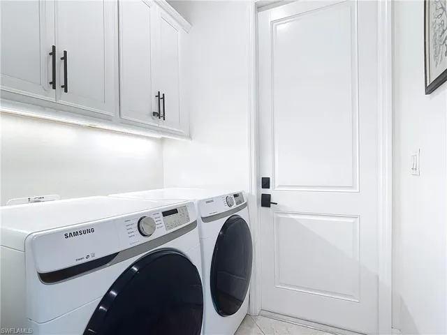 Washroom with light tile patterned floors, independent washer and dryer, and cabinets