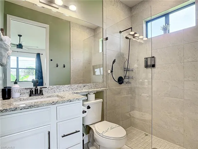 Bathroom with walk in shower, vanity, toilet, and ceiling fan