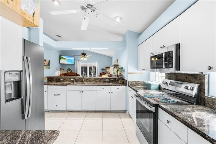 Kitchen with stainless steel appliances, vaulted ceiling, a ceiling fan, white cabinetry, and dark stone countertops