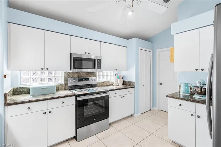 Kitchen featuring stainless steel appliances, white cabinets, ceiling fan, light tile patterned floors, and tasteful backsplash