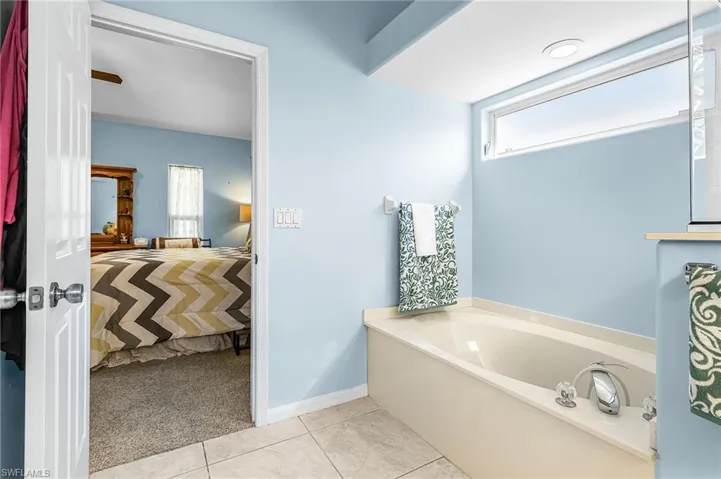 Ensuite bathroom featuring a garden tub, light colored carpet, and light tile patterned floors