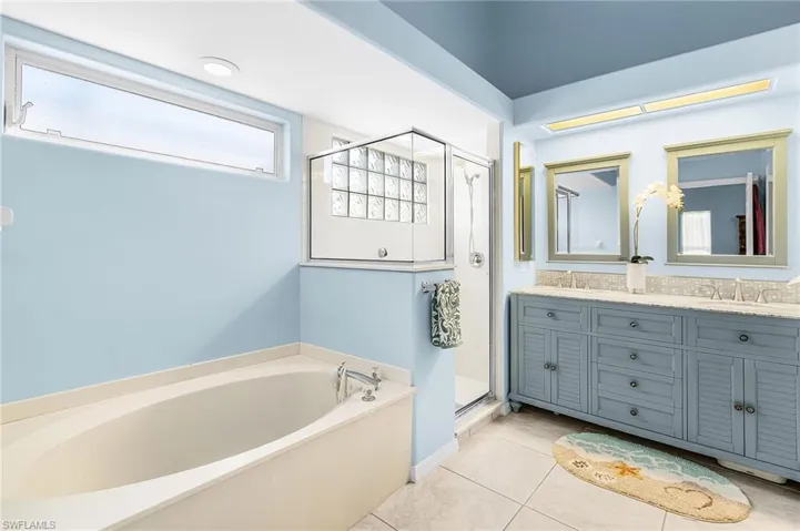 Bathroom with double vanity, a shower stall, a bath, and light tile patterned floors