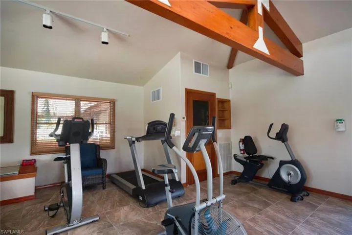 Workout room with lofted ceiling with beams and track lighting