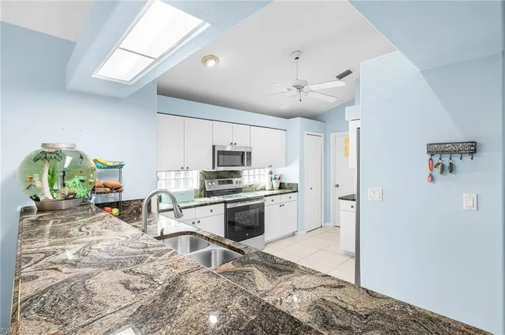 Kitchen with white cabinetry, stainless steel appliances, a ceiling fan, dark stone countertops, and vaulted ceiling