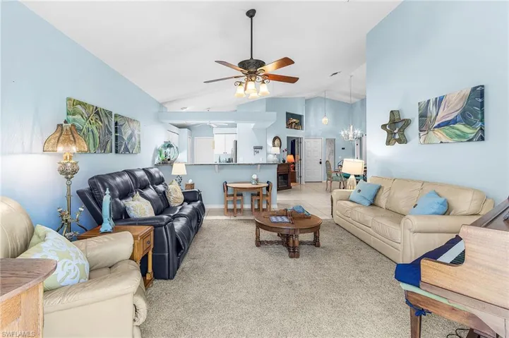Living area featuring a ceiling fan, vaulted ceiling, and light carpet