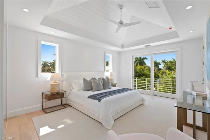 Bedroom with light wood-type flooring, multiple windows, a raised ceiling, a ceiling fan, and recessed lighting