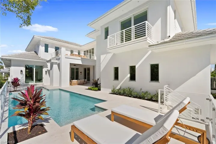 Back of house featuring a balcony, a patio area, an outdoor pool, and stucco siding