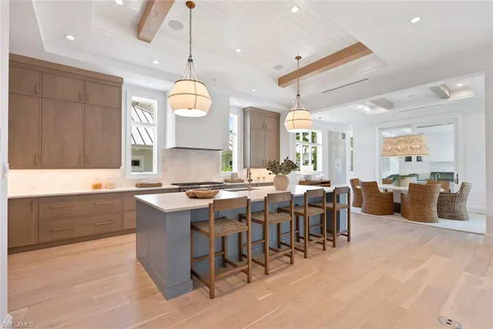 Kitchen featuring hanging light fixtures, a kitchen bar, an island with sink, light wood-style floors, and beamed ceiling