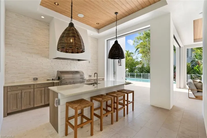 Kitchen with wooden ceiling, brown cabinets, a kitchen breakfast bar, light stone counters, and an island with sink