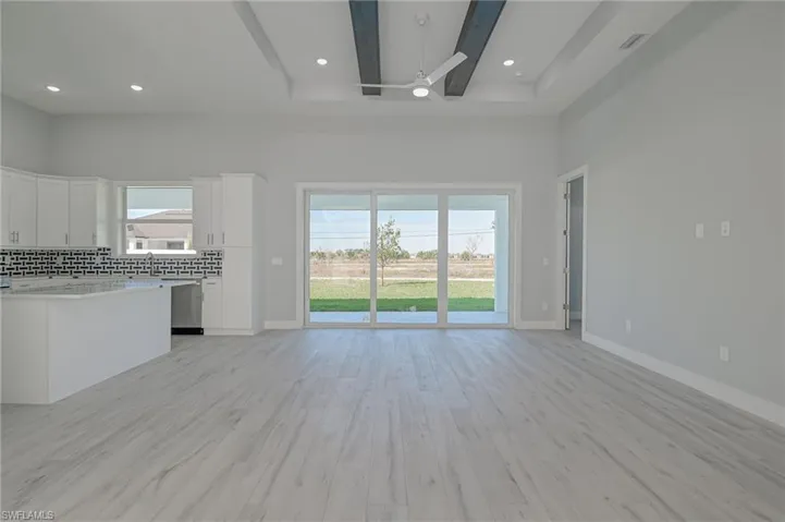 Unfurnished living room featuring a high ceiling, beam ceiling, light hardwood / wood-style floors, and a wealth of natural light