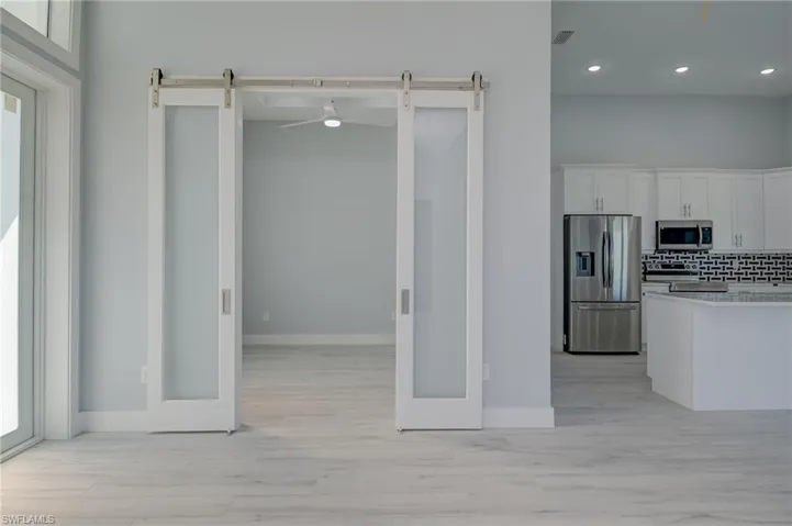 Kitchen featuring decorative backsplash, stainless steel appliances, white cabinets, and a barn door