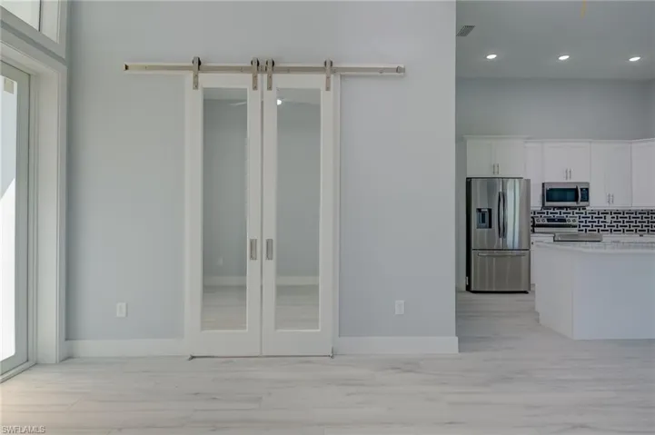 Kitchen featuring tasteful backsplash, light hardwood / wood-style flooring, white cabinetry, stainless steel appliances, and a barn door