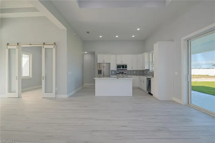 Kitchen with a center island, white cabinets, a barn door, backsplash, and appliances with stainless steel finishes