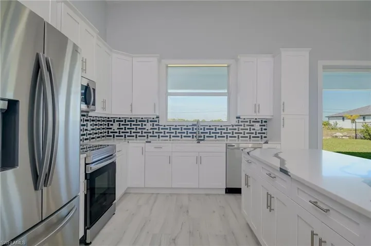 Kitchen with appliances with stainless steel finishes, white cabinetry, and a healthy amount of sunlight