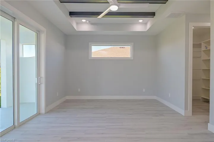 Unfurnished room featuring ceiling fan, light wood-type flooring, and a tray ceiling