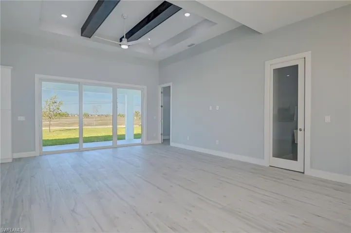 Spare room with beamed ceiling, light hardwood / wood-style flooring, a towering ceiling, and a raised ceiling