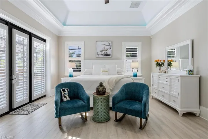 Bedroom with light hardwood / wood-style floors, a raised ceiling, access to outside, and multiple windows