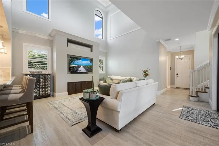 Living room featuring light wood-type flooring, crown molding, a towering ceiling, and a chandelier