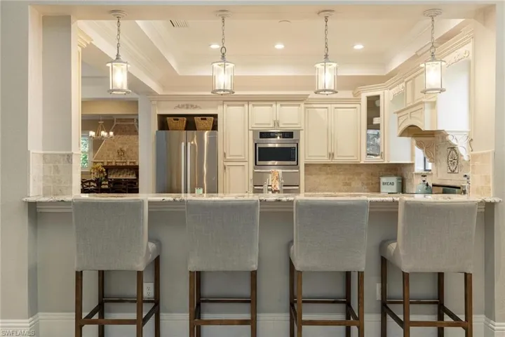 Kitchen featuring light stone countertops, stainless steel appliances, kitchen peninsula, decorative backsplash, and a breakfast bar