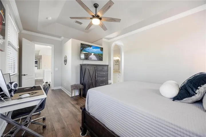 Bedroom featuring ornamental molding, a tray ceiling, ceiling fan, connected bathroom, and dark hardwood / wood-style floors