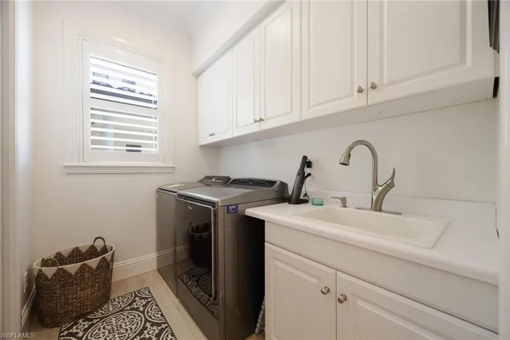 Washroom with cabinets, crown molding, sink, washing machine and dryer, and light hardwood / wood-style floors