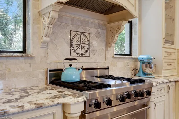 Kitchen with cream cabinetry, decorative backsplash, light stone counters, and high end range
