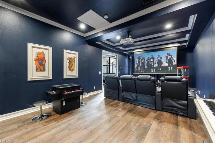 Home theater room featuring beam ceiling, crown molding, and light wood-type flooring