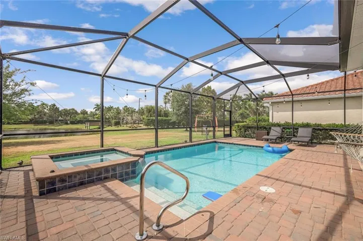 View of pool featuring a patio area, glass enclosure, a pool with connected hot tub, and a water view