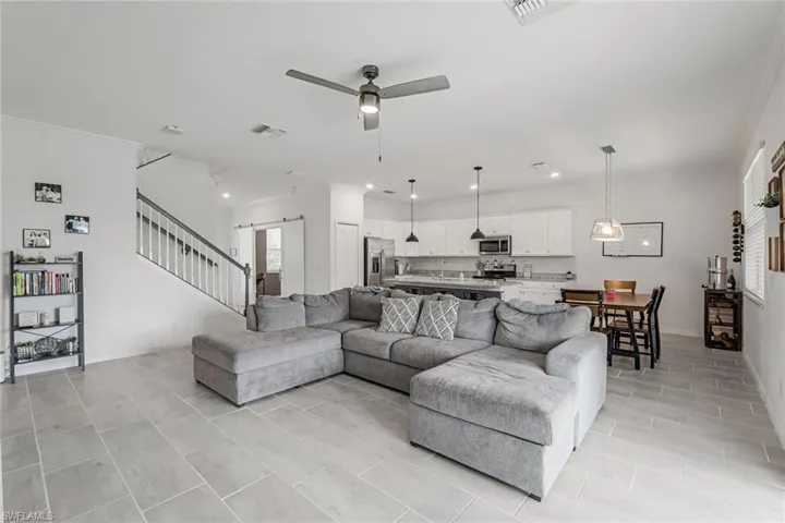 Living room featuring crown molding, visible vents, a ceiling fan, and stairs