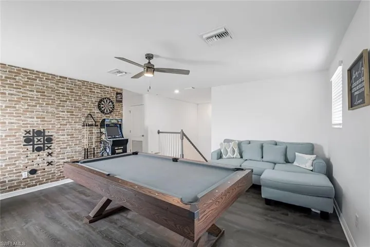 Rec room featuring brick wall, baseboards, wood finished floors, and visible vents