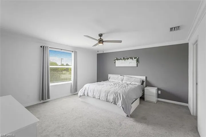 Carpeted bedroom with visible vents, crown molding, baseboards, and ceiling fan
