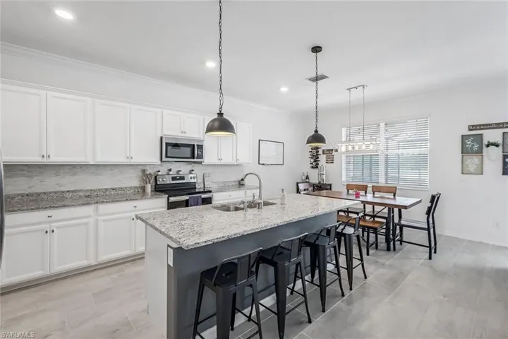 Kitchen with a kitchen breakfast bar, stainless steel appliances, visible vents, a sink, and white cabinetry