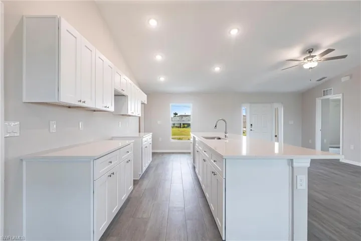 Kitchen featuring a ceiling fan, wood finished floors, a center island with sink, white cabinetry, and recessed lighting