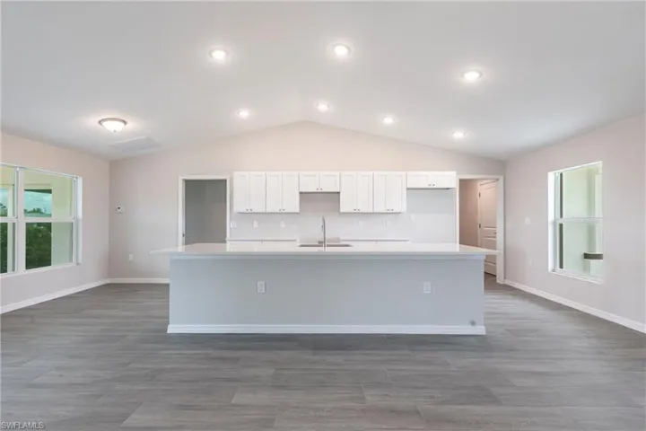 Kitchen featuring a large island with sink, white cabinets, lofted ceiling, light countertops, and dark wood-style floors