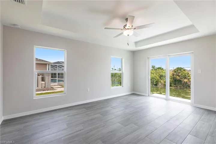 Spare room with a tray ceiling, a ceiling fan, and wood finished floors