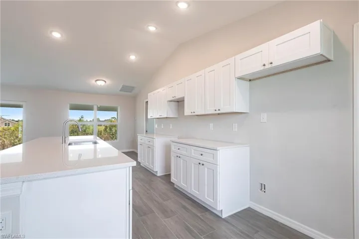 Kitchen with white cabinetry, wood finished floors, a center island with sink, light countertops, and recessed lighting
