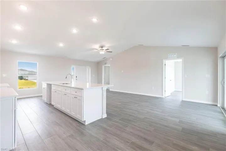 Kitchen with ceiling fan, light countertops, an island with sink, light wood finished floors, and vaulted ceiling