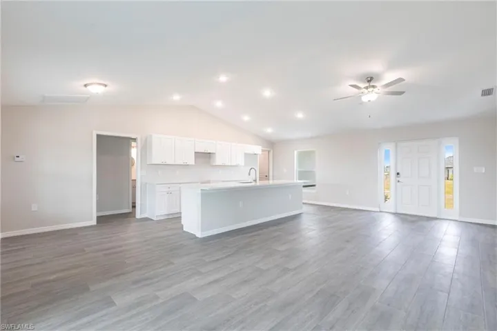 Unfurnished living room featuring vaulted ceiling, a ceiling fan, and light wood-style floors