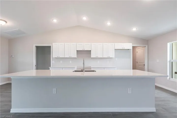 Kitchen featuring a large island, white cabinetry, lofted ceiling, dark wood-style floors, and light countertops