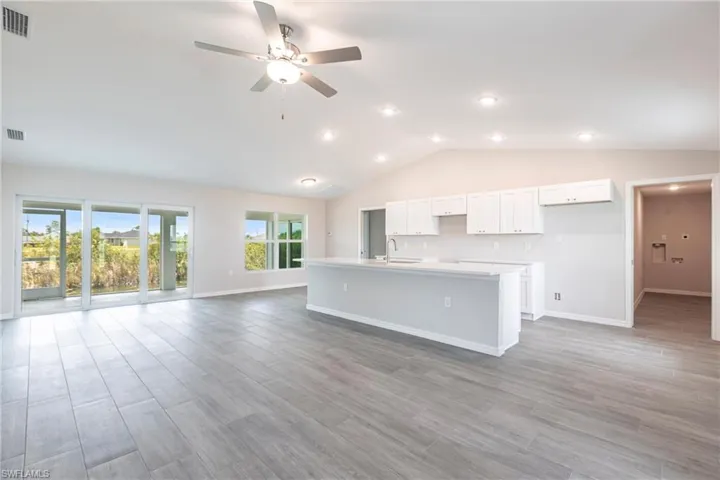 Kitchen featuring open floor plan, an island with sink, ceiling fan, white cabinets, and light countertops