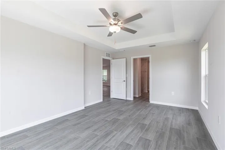 Unfurnished bedroom with a raised ceiling, wood finished floors, and a ceiling fan