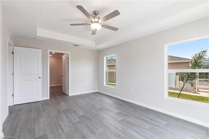 Unfurnished bedroom featuring a raised ceiling, wood finished floors, and ceiling fan