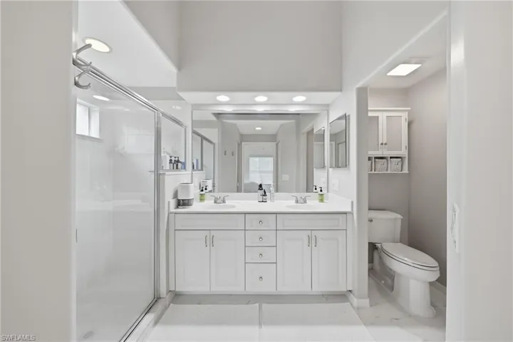 Bathroom featuring a dual vanity with white cabinetry, a glass-enclosed shower, a private water closet, and recessed lighting