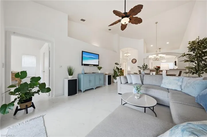 Spacious living area featuring high vaulted ceilings, large white porcelain tile flooring, an arched doorway, and an overhead tropical-style ceiling fan with integrated lighting